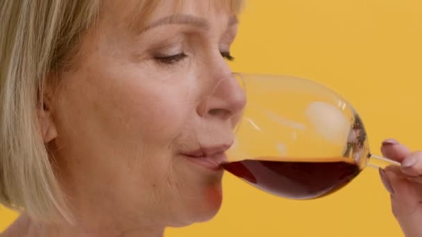 Frumoasă femeie în vârstă care bea vin roșu din sticlă pe fundal galben — Videoclip de stoc