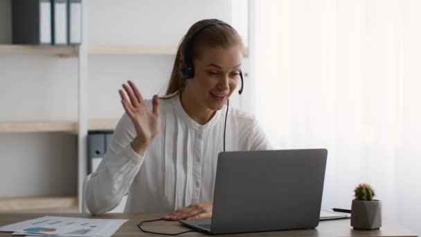 Videollamada. Mujer de negocios sonriente en auriculares que tiene teleconferencia en el ordenador portátil en la oficina — Vídeos de Stock