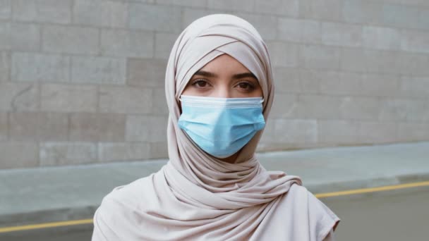 Young muslim woman woman wearing hijab and protective medical mask looking at camera outdoors, tracking shot — Stock Video