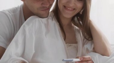 Gelecekteki ebeveynler. Mutlu Genç Eşler Pozitif Hamilelik Testine Bakıyor ve Kucaklıyor