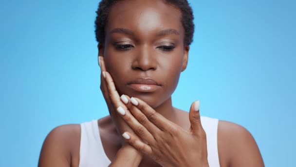 Dolor de muelas. Mujer afroamericana joven que sufre de dolor dental, tocando su mejilla inflamada, fondo azul — Vídeo de stock