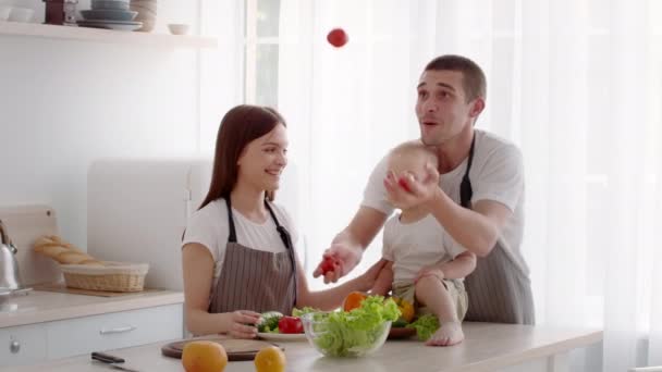 Οικογένεια με το μικρό μωρό μαγείρεμα μαζί στην κουζίνα, ο μπαμπάς ζογκλέρ με ντομάτες — Αρχείο Βίντεο