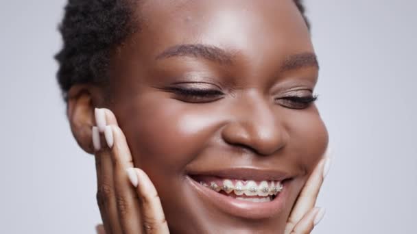 Jeune belle femme afro-américaine heureuse avec des appareils dentaires caressant son visage, appréciant la fraîcheur et la beauté — Video