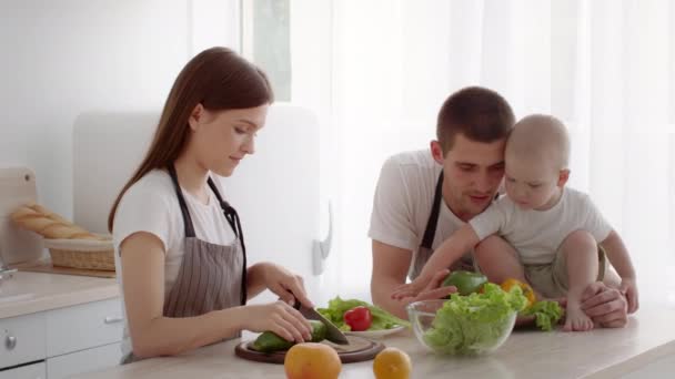 幼児の赤ちゃんと一緒にキッチンで健康的な料理を調理する若い家族 — ストック動画
