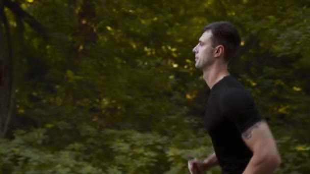 Kardiyo eğitimi. Kenar görüşlü genç kaslı adamın şehir parkında koşarken çekilen fotoğrafı, sabah koşusunun keyfini çıkarıyor. — Stok video