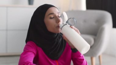 Yorucu bir ev işi. Şişeden su içen ve terli alnını silen yorgun, genç Müslüman bayan.