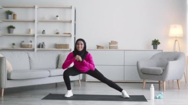 Ev pilatesi. Genç, aktif, orta doğulu, spor takım elbiseli ve evde esneyen geleneksel başörtüsü takan bir kadın.