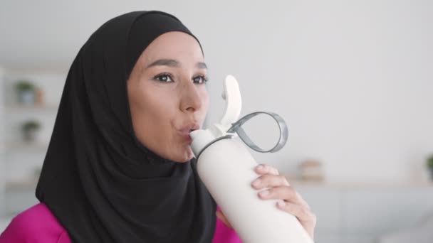 Waterbalans en sport. Close-up portret van positieve moslim dame in hijab drinkwater na fitness, vrije ruimte — Stockvideo