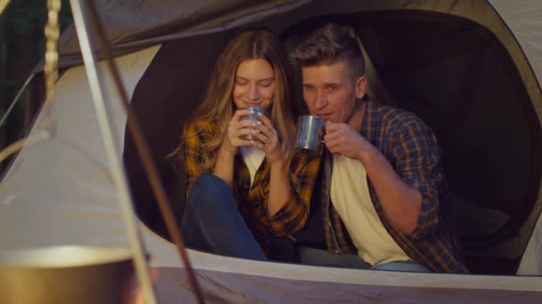 Молода щаслива пара туристів п'є гарячий чай і спостерігає за багаттям, насолоджується романтичним вечором у наметі, повільним рухом — стокове відео