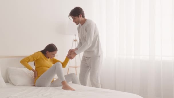 Ung kärleksfull make hjälpa sin gravida fru att stå upp från sängen och promenera med henne hemma, ta hand om henne — Stockvideo