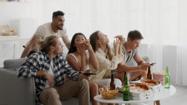Мультиэтнические друзья тысячелетия едят пиццу и пьют пиво дома — стоковое видео