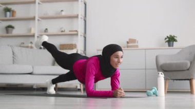 Güç egzersizi. Genç Ortadoğu İslamcı kadın tesettür takıyor tahta pozisyonu alıyor ve bacaklarını kaldırıyor.
