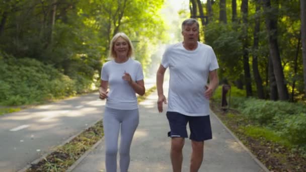 Un entraînement sain. Homme et femme âgés actifs courant ensemble dans le parc public, prenant des pauses et respirant — Video