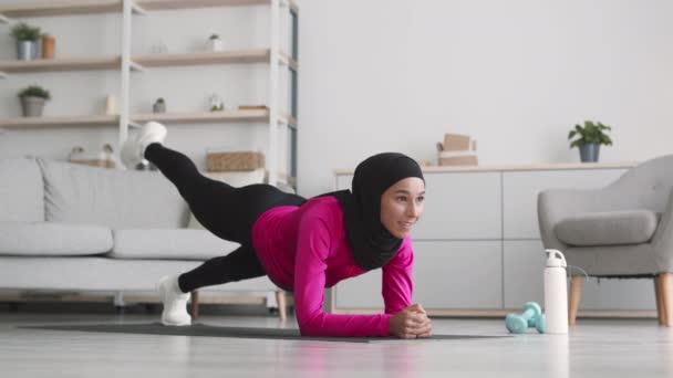 Entrenamiento de fuerza. Joven dama islámica del Medio Oriente usando hijab de pie en posición de tablón y levantando sus piernas — Vídeo de stock