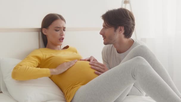 Worried husband comforting his pregnant wife, woman suffering from acute pain, lying on bed at home — Stock Video