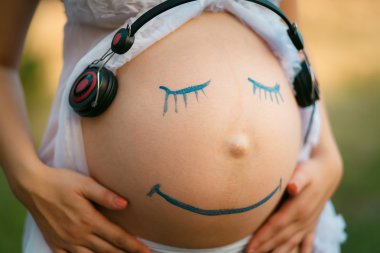 Pregnant woman belly closeup with smiling funny face drawing on  clipart