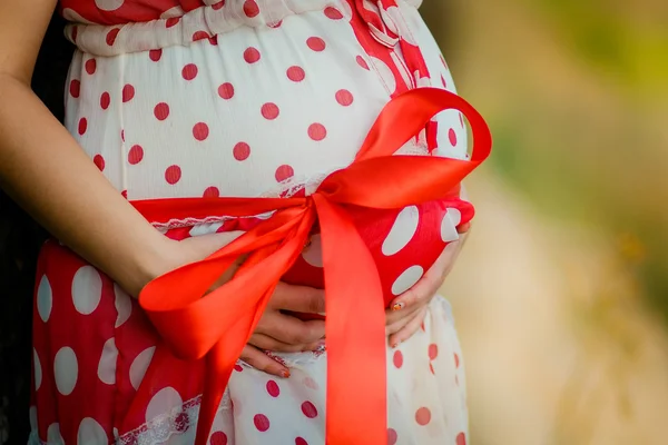 Embarazada mujer vientre primer plano con un gran lazo de cinta roja —  Fotos de Stock
