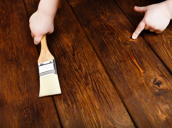 Babyhand trägt Schutzlack auf einem Holztisch auf — Stockfoto