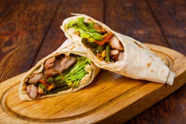 Burritos with chicken and vegetables at wooden desk