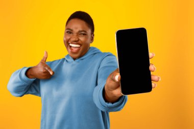 Şişman Afrikalı Kadın Kameraya Boş Telefon Ekranı Gösteriyor, Cep Telefonu Uygulama Uygulaması Sarı Arkaplan Üzerinde Akıllı Telefon Pozunu Gösteriyor. Stüdyo Çekimi