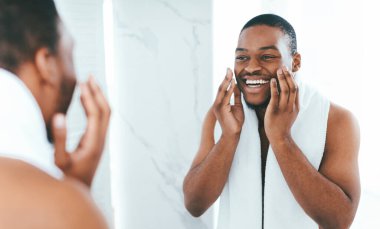 Tıraş losyonu. Banyoda hazırlanan mutlu gömleksiz zenci portresi, boynunda havluyla yakışıklı Afrikalı Amerikalı bir adam, evde günlük temizlik yapıyor, seçici bir odak noktası var.