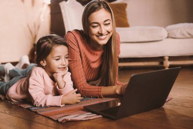 Sevimli genç anne ve kız oturma odasında dizüstü bilgisayar kullanıyor, birlikte vakit geçiriyorlar, mutlu anne ve çocuk çizgi film seyrediyor, oyun oynuyor ya da video sohbeti yapıyor, bedava fotokopi çekiyor.