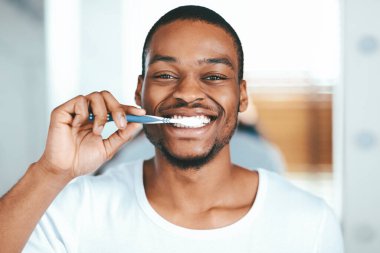 Evde diş fırçasıyla diş fırçalayan ve kameraya gülümseyen neşeli Afrikalı Amerikalı adam, evde günlük diş bakımı yapan mutlu siyah erkek, fotokopi uzayıyla yakın portre.