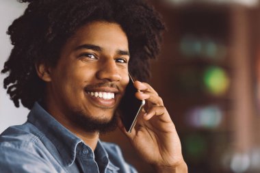 Cafe 'de cep telefonuyla konuşan Afrikalı Amerikalı bir gencin portresi, Milenyum siyahi yakışıklı bir adamın keyifli cep telefonu sohbetinden hoşlanması, seçici bir odak noktasıyla yakın çekim yapması ve boşluğu kopyalaması.