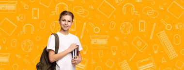 Neşeli bir çocuk okul ikonlarıyla dolu canlı sarı bir arkaplan önünde kitaplar ve sırt çantasıyla poz veriyor. Ortam neşeli bir okul atmosferini yansıtıyor..