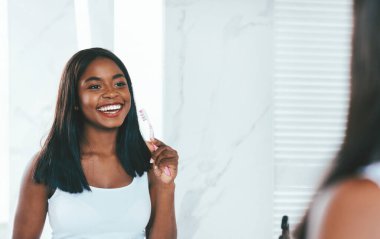 Sabah Temizliği Konsepti. Banyoda dişlerini fırçalayan neşeli siyah kadın diş fırçası ve diş macunu kullanan Afrika kökenli Amerikalı genç kadın diş sağlığı için seçici olarak yansımaya odaklanıyor.