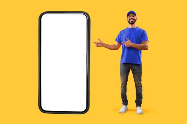 Arap Teslimatçı Adam, Sarı Arkaplan 'da Büyük Cep Telefonu Reklamcılık Online Kurye Servisi Uygulamasını Büyük Cep Telefonu Ekran Ekranında Gösteriyor. Telefonun yanında duran adam teslimat uygulamasını gösteriyor