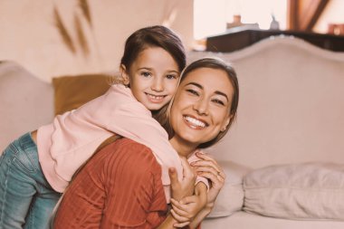Mutlu anne ve kızın kucaklaşan ve gülümseyen portresi, güzel genç bir kadın ve küçük bir kız çocuğunun oturma odasında kucaklaşması, kameraya poz vermesi, bedava fotokopi alanı.