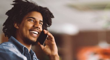 Mobil çağrı. Kapalı çekimde, kafede cep telefonuyla konuşan gülümseyen siyahi bir adam mutlu bir Afrikalı genç adamın portresi, güzel bir telefon konuşması, kopyalama alanı olan seçici bir odak noktası.