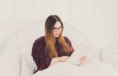 Pazar sabahı yatakta. Genç kadın sörf internet onun tablet pc, kopya alanı