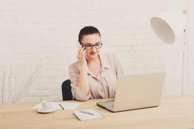 Orta yaşlı iş kadını ofiste smartphone. Kadın dizüstü bilgisayar kullanan ve işyerinde, kopya alanı cep telefonunda konuşuyor. İletişim kavramı