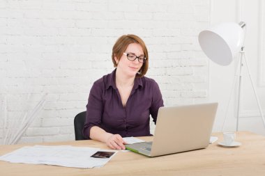 Orta yaşlı kadın ofiste. Dizüstü bilgisayar ve smartphone kullanarak kadın mimar. Ofis çalışanı. Kızıl saçlı Kafkas kadın bilgisayar ile koruyucu gözlük. Yüksek-key, yumuşak sesi.