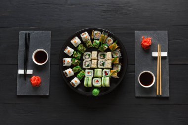 Japon restoranı, suşi rulo rustik ahşap arka plan siyah ve siyah arduvaz levha plakalı üstten görünüm... İki kişilik yemek çubukları, zencefil, soya, wasabi ile ayarla.