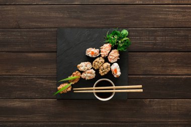 Japanese restaurant, gunkan sushi platter top view on rustic wood background and black slate plates.. Set with chopsticks, ginger, soy, wasabi.