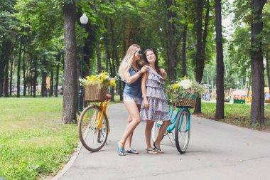 Mutlu Boho şık stil kızları eğleniyor. Bisikletleri ve sepetleri yabani çiçeklerle dolu güzel kadınlar..