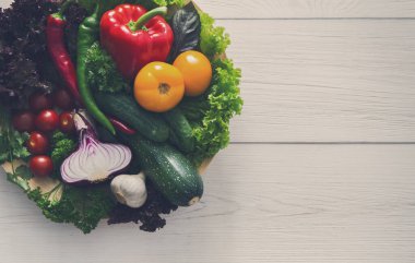 Bowl of fresh organic vegetables and greens on white wood background. Healthy natural food abundance on plate with copy space. Tomato, lettuce, carrot and other cooking ingredients top view