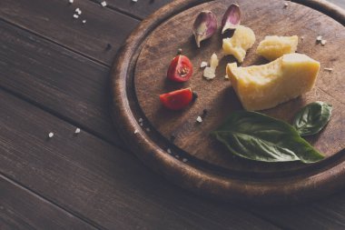 Peynir delikatessen baclground, closeup rustik ahşap üzerine. Sarımsak, domates ve fesleğen ile dekore edilmiş parmesan kesim ile ahşap masa