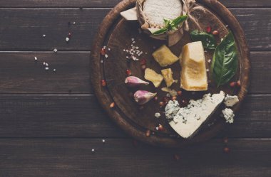 Cheese delikatessen top view on rustic wood. Blue cheese roquefort, parmesan, camembert and brie cuts decorated with garlic, pomegranate and basil, french cuisine ingredients