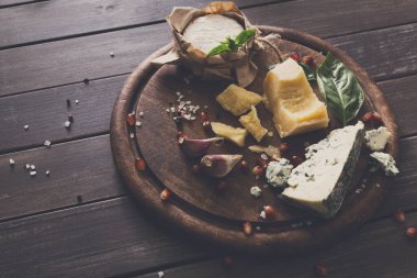 Cheese delikatessen on rustic wood. Blue cheese roquefort, parmesan, camembert and brie cuts decorated with garlic, pomegranate and basil, french cuisine ingredients