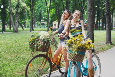 Yaz parkında kır çiçekleriyle bisiklete binen genç kızlar.