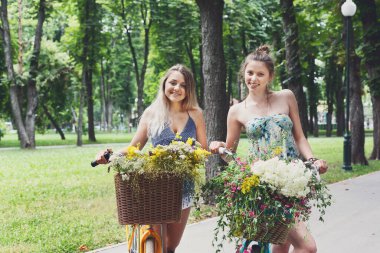 Bisiklet kır çiçekleri, closeup ile genç kızlar. Arkadaşlar, gençlik ve mutluluk, etkin yaz eğlence parkı kavram.