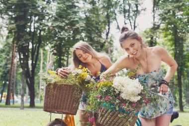 Bisiklet kır çiçekleri, closeup ile genç kızlar. Arkadaşlar, gençlik ve mutluluk, etkin yaz eğlence parkı kavram.