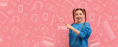 Saçları örgülü neşeli bir çocuk renkli bir okul temalı kolajın önünde duruyor. Okul malzemelerinin ve teknolojinin canlı görüntülerine işaret ederek meşgul ve heyecanlı..