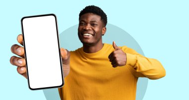 Sarı kazaklı neşeli bir adam elinde boş ekranlı bir akıllı telefon tutuyor ve başparmağını kaldırıyor. Renkli arka plan onun neşeli ifadesini arttırır..