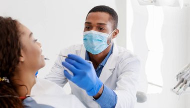 Afro-Amerikalı erkek stomatolog klinikte genç bayan dişlerini kontrol ediyor, panorama