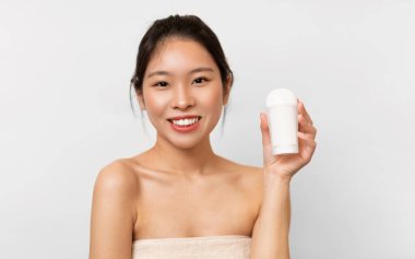 Reklam Kavramı. Gülümseyen Asyalı kadın elinde deodorant tüpü, kameraya yakın paket rulo gösteriyor, kozmetik ürünler sunuyor fotokopi alanı, beyaz stüdyo arka plan duvarı